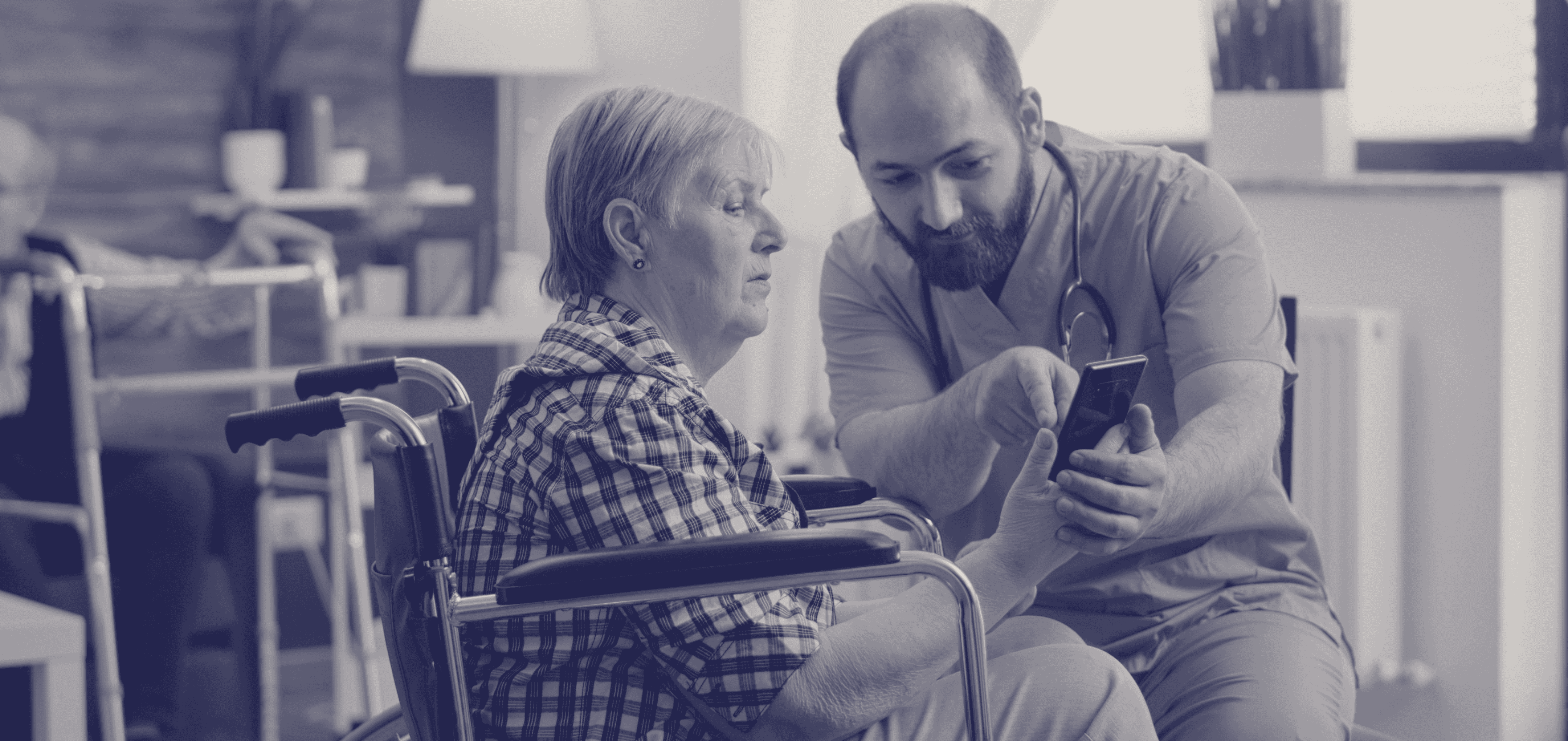 A healthcare professional wearing a stethoscope sits beside an elderly patient in a wheelchair, showing her something on a mobile device. The scene takes place in what appears to be a medical facility or care setting, with medical equipment visible in the background. The image has a blue-tinted filter overlay.
